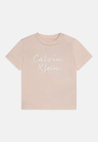 Halvány rózsaszín pamut póló rövid ujjakkal, amelyen a "Calvin Klein" logó fehér írással szerepel. Nyomógomb a bal vállnál az egyszerű öltözködés érdekében.