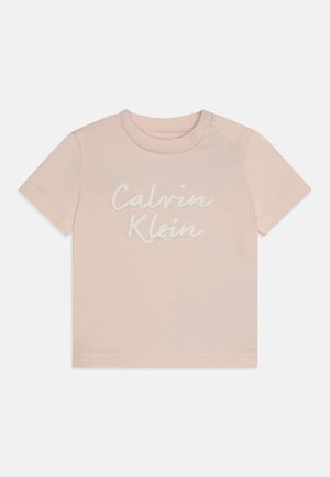 Camiseta de algodón de color rosa pálido con mangas cortas, que presenta el logo de "Calvin Klein" en letra blanca. Botón a presión en el hombro izquierdo para facilitar el vestido.