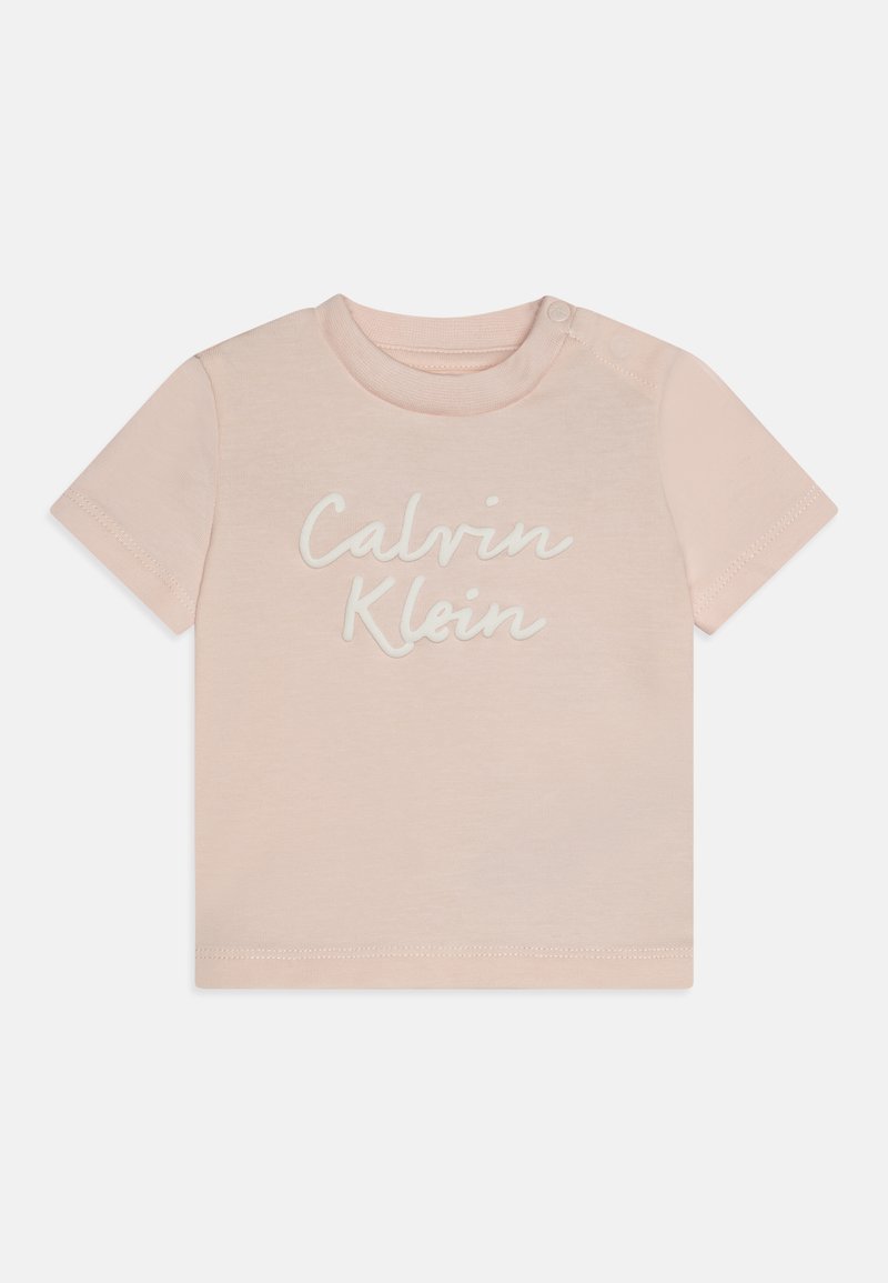 Halvány rózsaszín pamut póló rövid ujjakkal, amelyen a "Calvin Klein" logó fehér írással szerepel. Nyomógomb a bal vállnál az egyszerű öltözködés érdekében.
