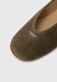 Green suede flat shoe featuring a rounded toe and a gold "COACH NEW YORK" logo on the side, with a smooth inner lining.
