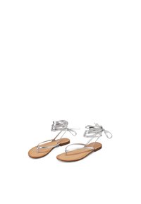 Sandali piatti metallici argento con design a strisce sottili, caratterizzati da una soletta nuda e legami alla caviglia. Texture liscia con un'estetica minimalista.