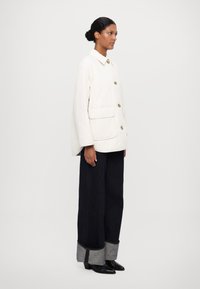White quilted jacket with a collar, featuring two front pockets and large buttons, paired with dark wide-leg jeans and heeled shoes.