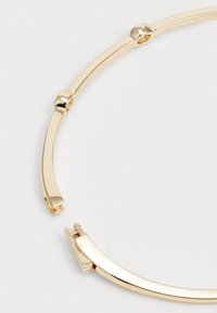 Gold-tone metal bracelet featuring a smooth, curved design with rounded joints and a secure clasp. Polished finish with subtle accents.