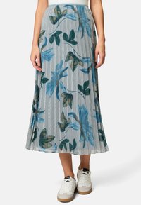 Plissé bloemenrok met een lichtblauw en grijs verticaal gestreept patroon, versierd met groene en bruine bladeren. Draagt wit sneakers.