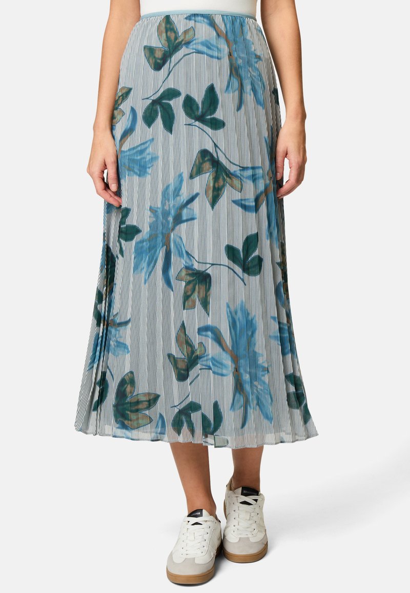 Plissé bloemenrok met een lichtblauw en grijs verticaal gestreept patroon, versierd met groene en bruine bladeren. Draagt wit sneakers.