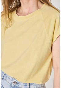 T-shirt giallo a maniche corte con scollo rotondo e vestibilità rilassata, realizzato in tessuto morbido, abbinato a pantaloni corti in denim blu chiaro.