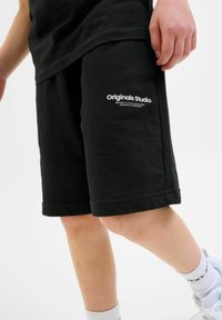 Crne pamučne šortse s opuštenim krojem. Sadrže bijeli tekstualni logo "Originals Studio" sa strane, glatku teksturu i ušiveno porub.