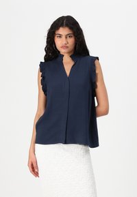 Blusa senza maniche blu navy con dettagli arricciati sulle spalle e scollatura a V, realizzata in tessuto leggero e con una vestibilità rilassata.