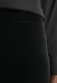 Jupe en velours noir avec une texture lisse, dotée d'une taille ajustée et d'une construction sans coutures. Accompagnée d'un haut en tissu sombre.