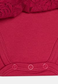 Body de bebé de algodón color burdeos con un borde de encaje en el escote y cierres de presión en la parte inferior. Textura suave, diseño de manga corta.