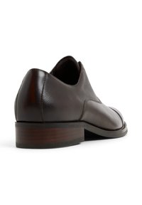 Scarpa in pelle marrone con finitura testurizzata, punta arrotondata e tacco in legno stratificato. Presenta un design elegante con dettagli di cucitura minimi.