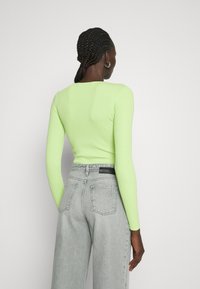 Langärmeliges, geripptes Oberteil in leuchtendem Limettengrün, kombiniert mit hochtaillierten, hellgrauen Jeans, die ein Gesäßpatch und zwei Gesäßtaschen haben.