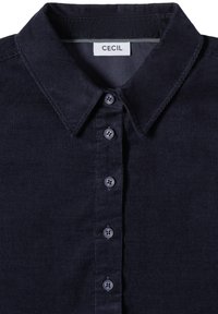 Chemise en velours côtelé bleu marine foncé avec un col classique et cinq boutons sur le devant, étiquetée "CECIL" à l'intérieur du col.