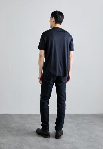Camiseta negra de manga corta hecha de una tela suave, combinada con jeans de mezclilla oscura y botines negros. Diseño simple sin logotipos.