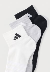 Tři páry kotníkových ponožek: bílé s černým logem, světlé šedé a černé. Žebrovaná textura, délka do poloviny lýtek, jemné vzory.