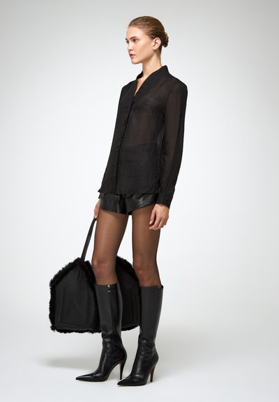 Camicia nera trasparente con colletto alla cinese, abbinata a pantaloni corti in ecopelle neri a vita alta e stivaletti alti con tacco.