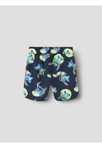 Shorts de bain bleus avec une ceinture élastique, ornés d'un motif coloré représentant un personnage de dessin animé, des planches de surf et des lunettes de soleil sur un fond bleu marine.