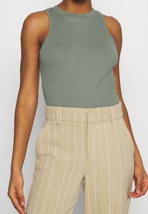 Geribd, mouwloos topje in gedempte groene stof met een ronde hals, gecombineerd met beige broek met verticale witte strepen.