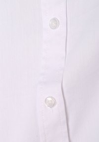 Primo piano di un tessuto di camicia bianca con una fila di bottoni di plastica trasparente e cuciture visibili lungo la patta. Tessuto liscio.