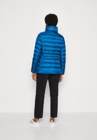 Blå puffjacka med hög krage, figursydd midja och horisontellt quiltat mönster. Bärs med svarta byxor och vita sneakers.