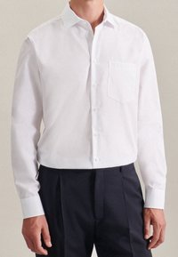 Vit skjorta med spetsig krage, en bröstficka, långa ärmar och en slät yta, kombinerad med mörka byxor.