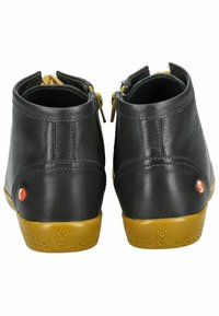 Botas de cuero negro hasta el tobillo con cremalleras amarillas, suelas de goma marrón y acentos de logo rojo en el talón y el lado. Textura suave y forma redondeada.