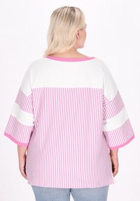 Lätt skjorta med en vit övre del och rosa vertikala ränder nedanför. Den har ärmar som når till armbågen och en rund halsringning.