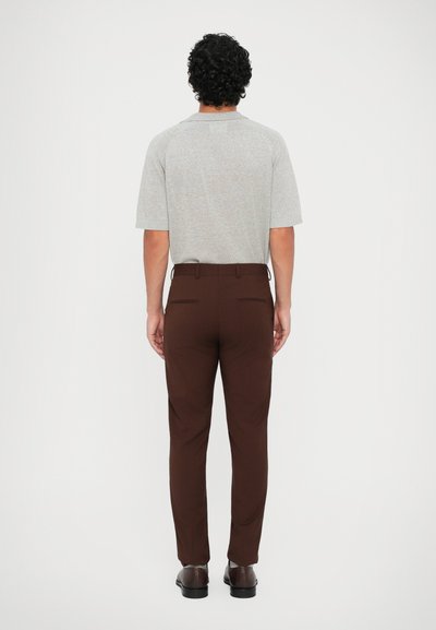 Cămașă tricotată gri cu mânecă scurtă, asortată cu pantaloni maro. Cămașa are guler; pantalonii au buzunare la spate și un croi adaptat.