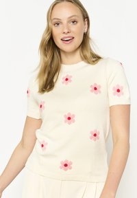 Knitted short-sleeve sweater in cream with pink flower patterns and red centers. Features a round neckline and ribbed hem.