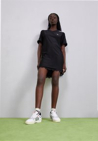 Black athletic dress with short sleeves, scalloped hem, and white stripe accents. Paired with white sneakers featuring green stripes.