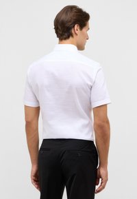 Korte mouwen witte blouse met een gestructureerde afwerking, voorzien van een klassieke kraag en een rechte snit, gecombineerd met zwarte broek en achterzakken.
