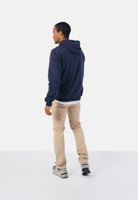 Marineblauwe fleece hoodie met een kangoeroezak en een capuchon met trekkoord, gecombineerd met beige broeken en grijze sneakers met zwarte accenten.