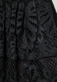 Tessuto di pizzo nero caratterizzato da intricati design ritagliati che richiamano foglie, con una texture stratificata e un motivo a rete geometrico.