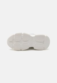 Semelle de sneaker blanche en caoutchouc avec un motif de bande de roulement texturé, dotée d'une fente centrale pour la flexibilité et d'un logo intégré sur le côté.
