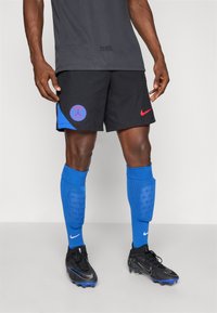 Black athletic shorts with blue and red accents, featuring a logo. Blue knee-high socks and black soccer cleats with blue details.