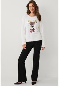 Wollen witte trui met een rendierontwerp en een rode strik. Gecombineerd met zwarte aansluitende broek en zwarte puntige schoenen.