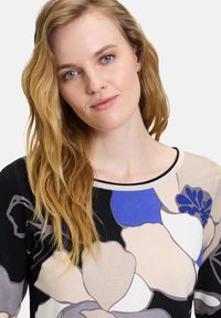 Strickpullover mit einem floralen Muster in Beige, Schwarz und Blautönen, mit einem klassischen Rundhalsausschnitt und langen Ärmeln.