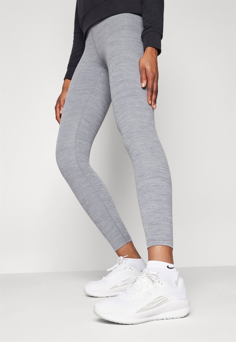 Grå leggings i stretchigt material med en melerad mönstring, ihop med vita träningsskor som har subtil branding.