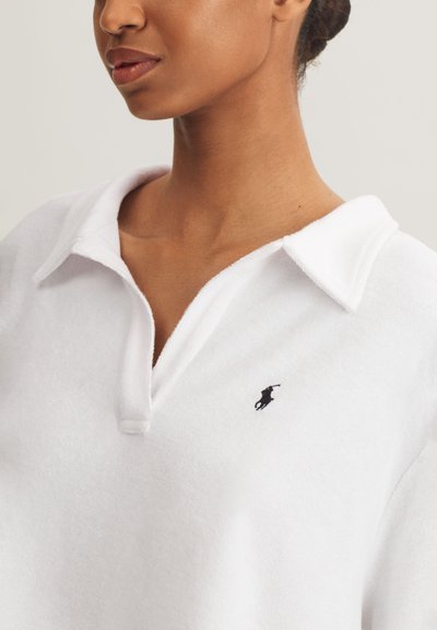 Λευκό πόλο μπλουζάκι από απαλό ύφασμα με γιακά και πατιλέτα με τρία κουμπιά· διαθέτει μικρό μαύρο λογότυπο στο αριστερό μέρος του στήθους.