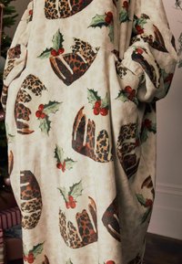 Oversize fleece-beklædning med en cremefarvet baggrund prydet med et mønster af brune leopardpletter og kristtornblade med røde bær.