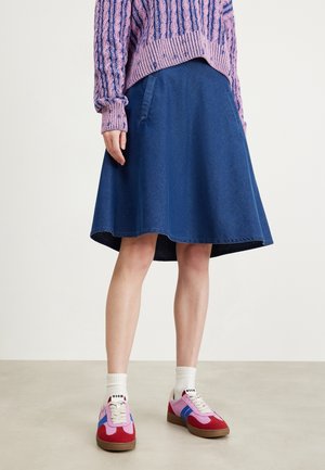 Person iført en blå denim A-line nederdel, lilla tekstureret sweater, hvide sokker og pink, røde og blå sneakers med gummisåler.