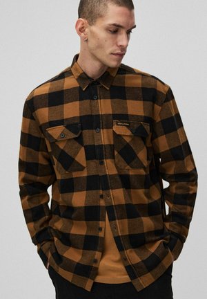 Brązowa i czarna koszula z flaneli w kratę z zapięciem na guziki, dwoma kieszeniami na piersi oraz metką marki na lewej kieszeni. Długie rękawy i luźny krój.
