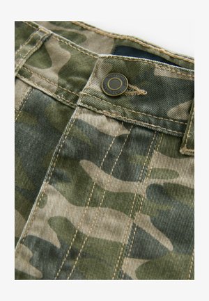 Zöld és bézs árnyalataiból készült, camouflázs mintás szövet, látható varrással, fémből készült gombbal és sima textúrával.