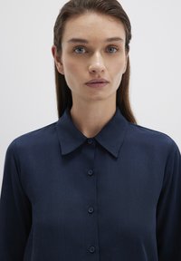 Navy blue button-up shirt featuring a spread collar, front placket with buttons, and long sleeves. Smooth texture and tailored fit.