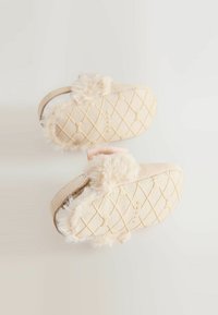 Chaussons pour bébé en beige doux avec un bord en fausse fourrure. Dotés d'une semelle texturée matelassée et d'une sangle élastique pour un maintien sécurisé.