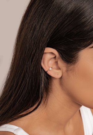 Silberner Steckerohrring mit floralem Design, ausgestattet mit einem kleinen, klaren Edelstein, der am äußeren Ohr befestigt ist, während das Haar teilweise das Ohrläppchen verdeckt.