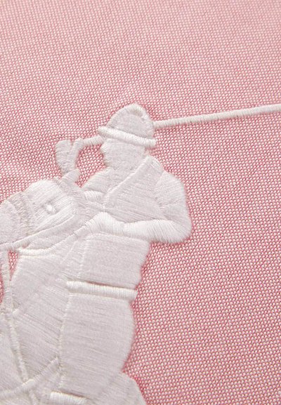 Λευκός γκολφέρ με κέντημα, που κουνάει μπαστούνι σε ροζ υφή φόντου.