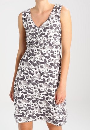 Femme portant une robe sans manches à col en V avec un motif floral noir et blanc sur un fond clair uni.