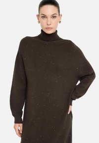Bruine coltrui van gebreide stof, met een losse pasvorm, lange mouwen en verspreide metallic spikkels voor extra detail.