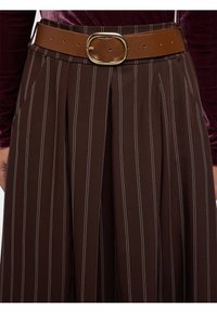 Pantaloni marroni a righe con strisce verticali bianche, caratterizzati da una cintura larga e una cintura in finta pelle marrone con una fibbia circolare dorata.